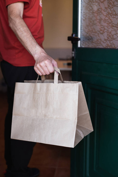 Un hombre recogiendo una bolsa de papel en la puerta de su casa. Compras en línea. Entrega a domicilio. Foto vertical. - Foto, Imagen