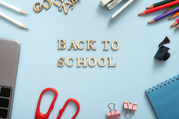 Back to school text with laptop, notebook and stationary on pastel blue background. Office desk flat lay. - Фото, изображение