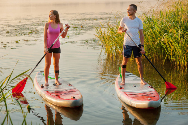 a young couple walks along the river on a paddle board., morning light - Foto, Imagen