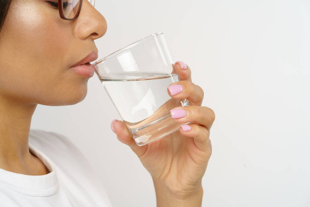 Gezond en gehydrateerd. Zijaanzicht van jonge Afro-Amerikaanse vrouw drinken zuiver mineraalwater terwijl geïsoleerd over grijze studio achtergrond. Behoud van vochtbalans en hydratatie concept - Foto, afbeelding