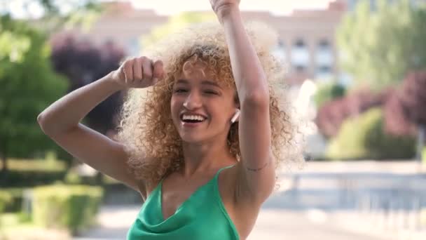 Portrait of young Brazilian woman wearing earphones listening music and dancing in a summer day. - Filmagem, Vídeo