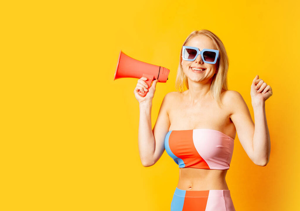 Stylish blond woman in colored swimming suit and megaphone on yellow background - Φωτογραφία, εικόνα