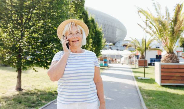 Krásná Starší žena v módní nosit čas na ulici pomocí smartphonu. Šťastný seniorský hovor v mobilu, teplý slunečný den. Urban concept, technology banner - Fotografie, Obrázek