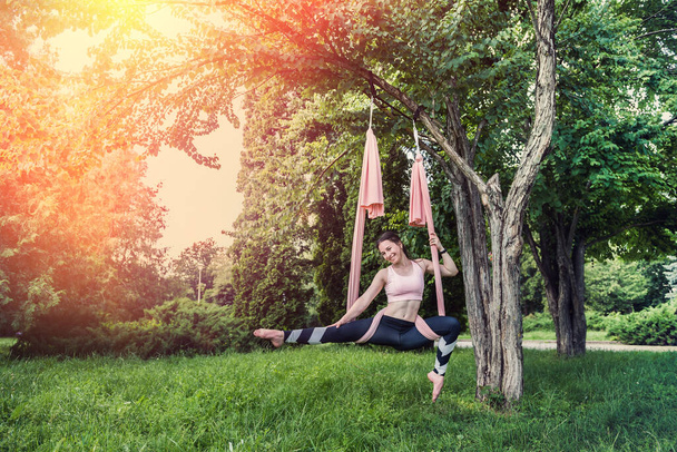 ein Mädchen mit schlanker Figur beschloss, bei schönem Wetter Yoga-Übungen im Freien zu praktizieren. Outdoor-Yoga-Fliegenkonzept am Baum - Foto, Bild