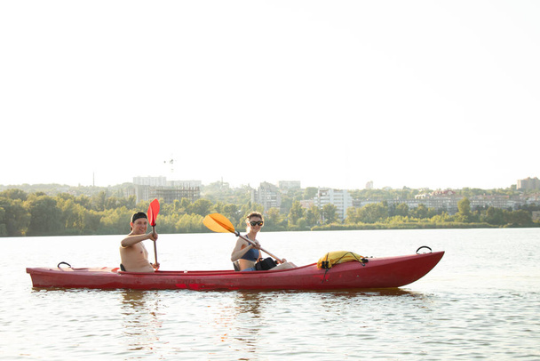 Uma menina e um cara estão navegando ao longo do rio Dnieper ao longo da cidade em uma canoa durante a guerra na Ucrânia 2022, canoagem, paisagem da cidade - Foto, Imagem