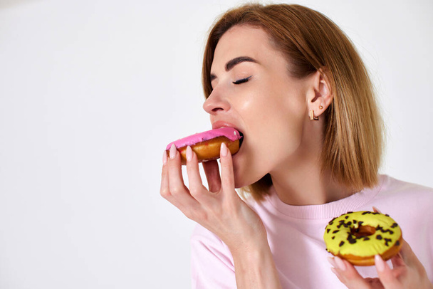 smiling beautiful blonde woman eating donuts with pleasure isolated on white background. copy space - Photo, Image