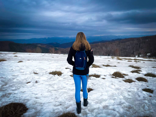 Woman with backpack hiking down a field covered in snow on a cloudy winter day - Photo, image