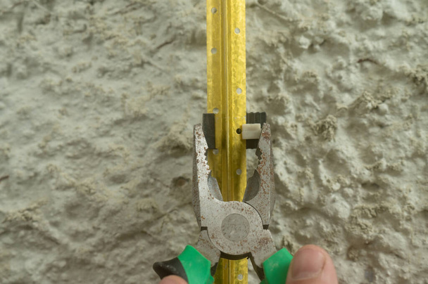 Metal guides for plastering walls, installation of metal beacons on the wall, pliers clamp the beacon holders. - Fotó, kép