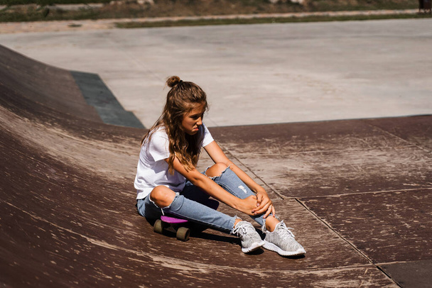 Active child girl after fall from penny board injured, sitting and feel pain on sport ramp on skate park playground - Photo, Image