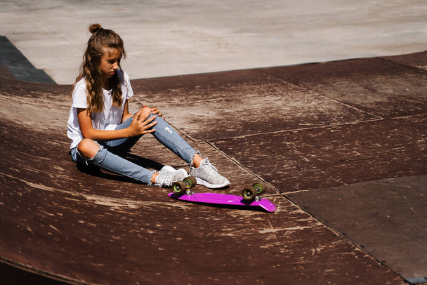 Active child girl after fall from penny board injured, sitting and feel pain on sport ramp on skate park playground - Fotó, kép