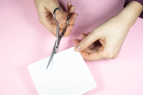 vrouw is snijden wit papier met schaar, close-up. - Foto, afbeelding