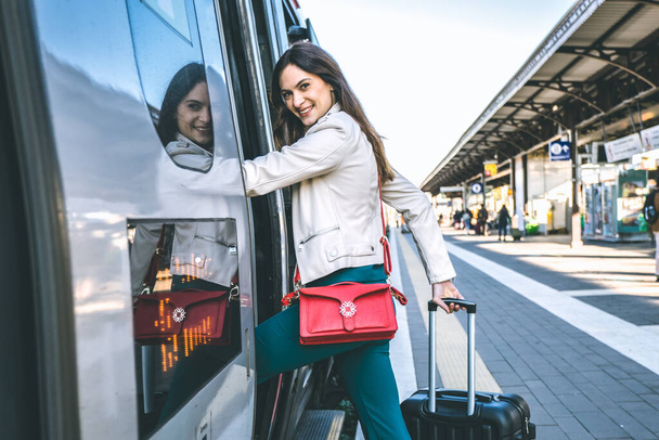 Young business woman standing on train door peeking out looking for somebody in railway station - Potrait of beautiful traveler woman getting on the train - Travelling concept - Photo, image