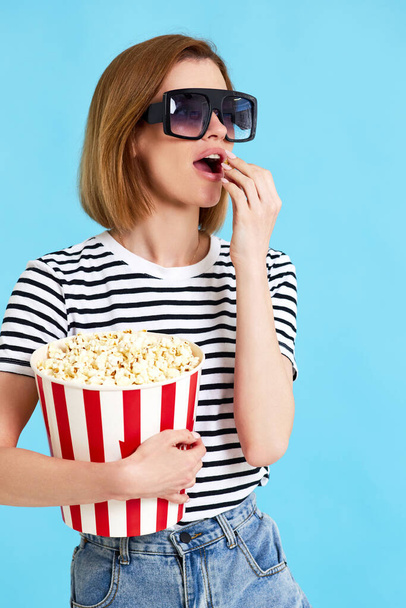 beautiful girl watching movie filmand eating popcorn isolated on blue background - 写真・画像