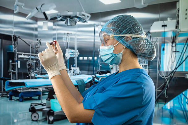 atrakcyjny doświadczony lekarz noszący jednolite rękawice ochronne do masek twarzy wykonujący analizy krwi pacjentów na sali operacyjnej w szpitalu - Zdjęcie, obraz