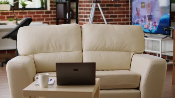 Sisustus moderni huoneisto sohvapöytä ottaa kannettava tietokone sitä. Tyhjä olohuone, jossa ei ole ketään ja mukava sohva ja pöytä, jonka päällä kannettava tietokone. - Materiaali, video