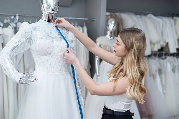female tailor use measure-tape for measure new wedding dress on mannequin in store - 写真・画像
