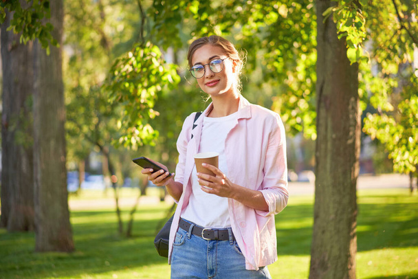 Businesswoman standing summer park Business person using smartphone Outdoors Successful european caucasian woman freelancer or teacher walking outside backpack dressed jeans white shirt pink jacket - Foto, Bild