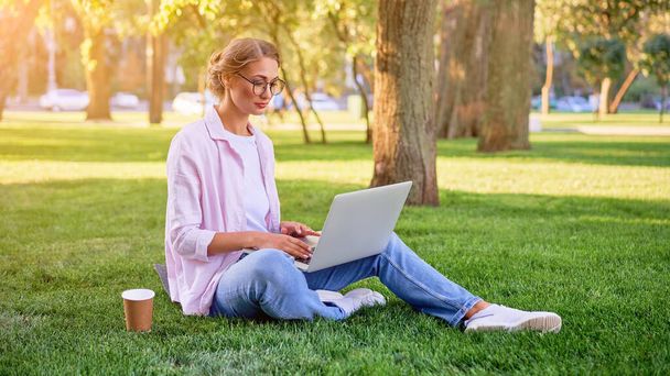 ラップトップを使用して草の夏の公園に座っているビジネスマンリモートで働くビジネス人。屋外成功したヨーロッパの白人女性のフリーランサーは、ビデオ通話教師の勉強仕事をオンラインレッスンを作る  - 写真・画像