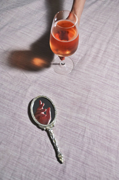 Mano abstracta en espejo vintage y mano de mujer sosteniendo copa de vino rosa - Foto, imagen