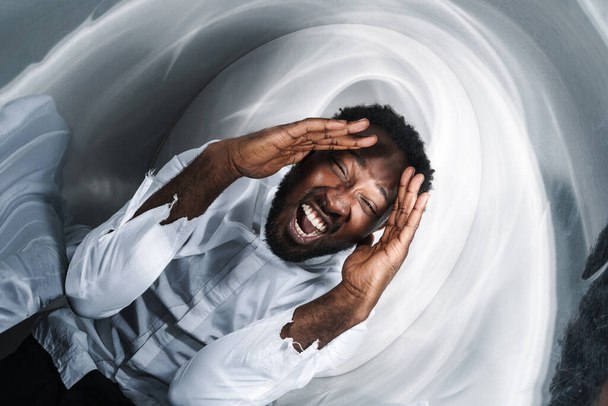 Young black man holding his head and screaming isolated over metal wall - 写真・画像