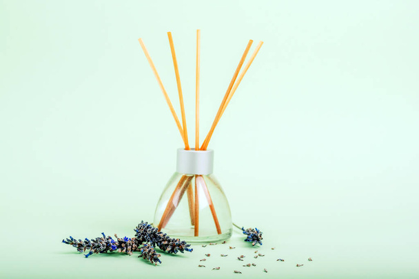 Glass bottle of reed diffuser and lavender blossom on light green background. Closeup. - Foto, imagen