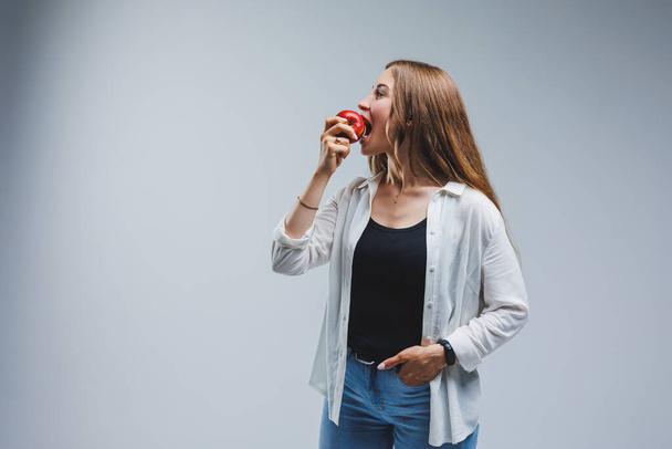 Cute brunette woman in white shirt holding red apple in hand standing on isolated white background dietetics and nutrition. Healthy food - Zdjęcie, obraz