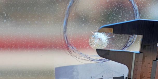 Op de plaats delict meet de wetenschappelijke politie het kaliber van het gat, achtergelaten door een kogelinslag in het glas van een raam. - Foto, afbeelding