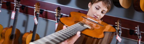 Музыкант смотрит на размытую акустическую гитару в музыкальном магазине, баннер  - Фото, изображение