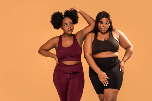 Two female friends posing in fashionable sporty clothes after workout. African women. Plus size. Body positive concept. Studio shot - Fotografie, Obrázek