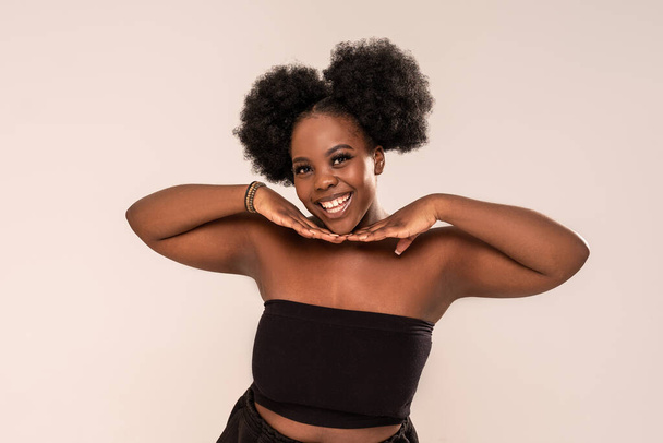 Young happy afro woman looking and smiling to the camera. Real people emotions. A lot of copy space on the grey studio background - Foto, Imagem