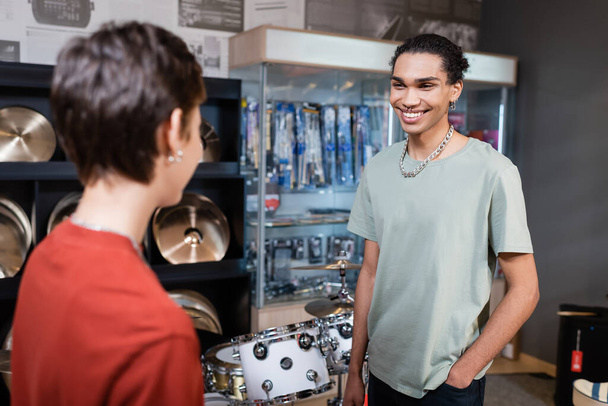 Smiling african american customer looking at blurred seller in music store  - Fotó, kép