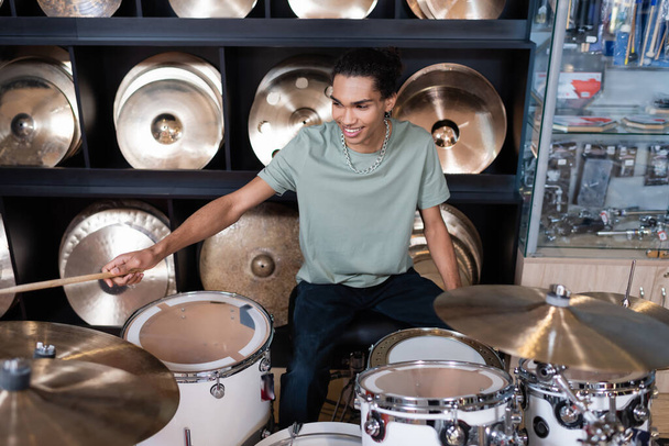 Smiling african american customer playing drums in music shop  - Fotó, kép