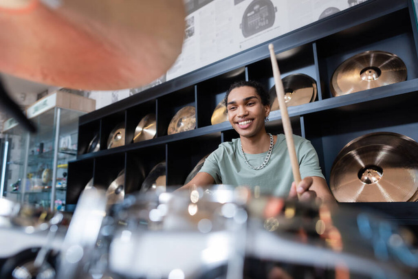 Улыбающийся африканский американец играет на размытых барабанах в музыкальном магазине - Фото, изображение
