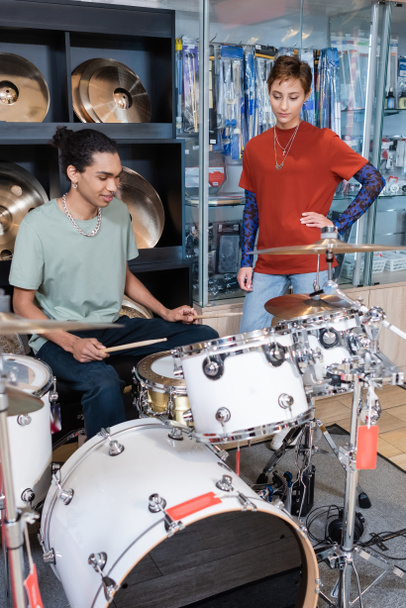 Seller standing near african american customer playing drums in music store  - Foto, imagen