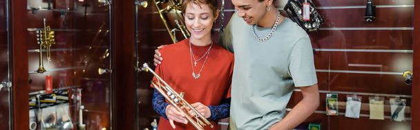 Young african american man hugging girlfriend and looking at trumpet in music store, banner  - Foto, imagen