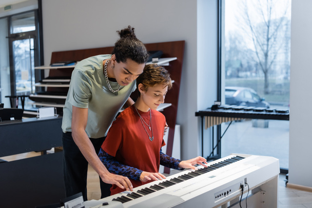 Young woman playing synthesizer with african american boyfriend in music store  - Foto, immagini