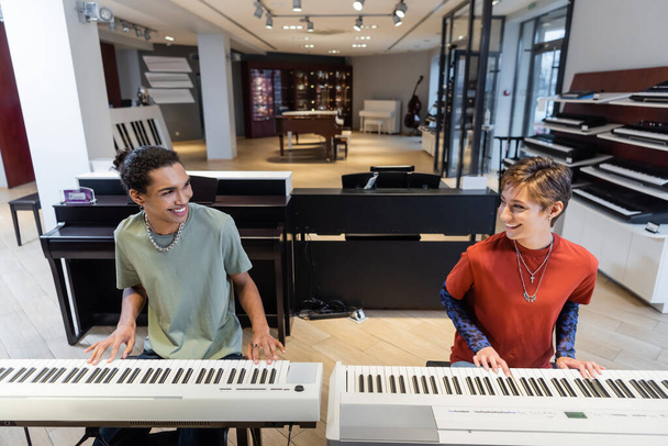 Positive multiethnic couple playing synthesizers in music shop  - Fotoğraf, Görsel