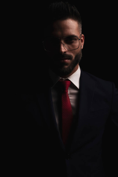 happy young man in elegant suit with glasses smiling and  posing in studio in front of black background - Foto, imagen