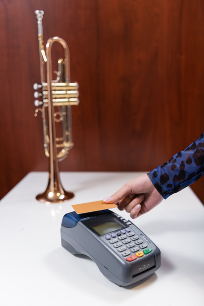 Обрезанный вид женщины, платящей кредитной картой возле размытой трубы в музыкальном магазине  - Фото, изображение