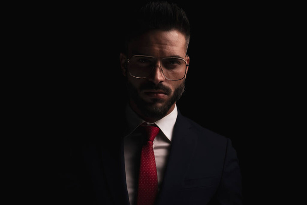 portrait of handsome businessman with glasses wearing elegant suit and posing in front of black background in studio - Foto, imagen