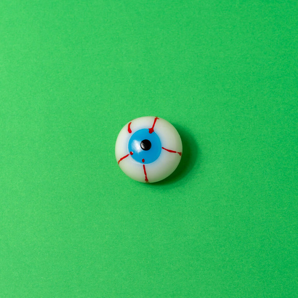 Bloody eyeball on a vivid green background. Minimal Halloween concept. - Photo, image