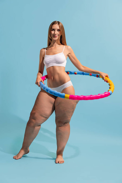 Motivation to be beautiful and healthy. Young slim girl with plus-size womans body doing exercises with hula hoop isolated on colored background. Weight loss, fitness, healthy eating, active life - Foto, Imagem