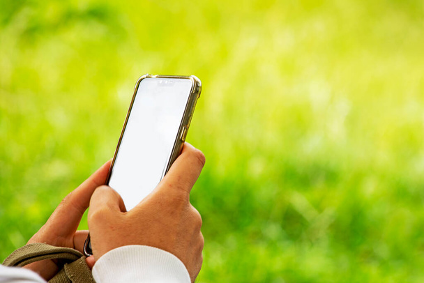 man hold white smartphone lying on grass at picnic. Smartphone template for advertising - Фото, зображення