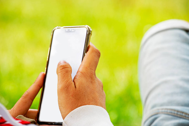 hombre mantenga teléfono inteligente blanco acostado en la hierba en el picnic. Plantilla Smartphone para publicidad - Foto, imagen
