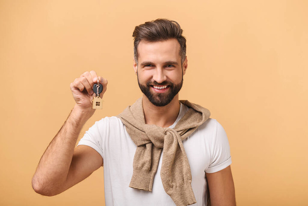 Jovem feliz mostrando chaves de pé isolado no bege, homem feliz com chaves, conceito realocado - Foto, Imagem