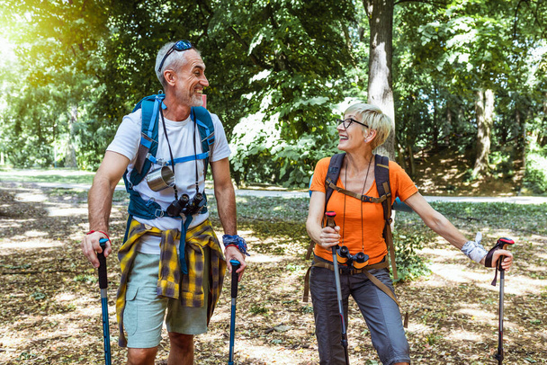 Senior couple hiking in forest wearing backpacks and hiking poles. Nordic walking, trekking. Healthy lifestyle. - Photo, Image
