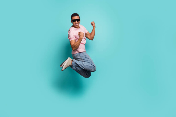 Full length photo of lucky excited man dressed pink t-shirt rising fists jumping high isolated turquoise color background. - Valokuva, kuva