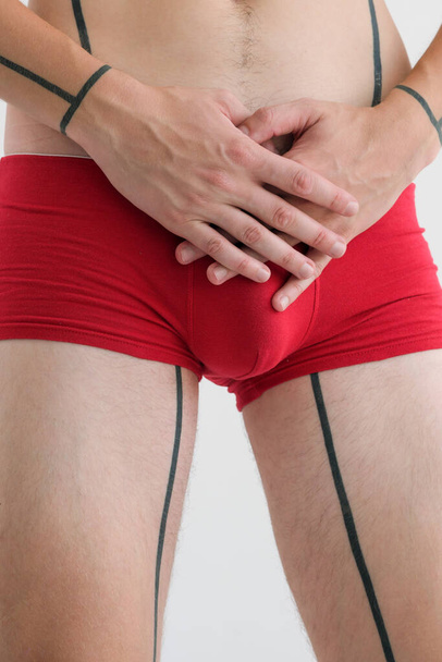 The hands of a young guy in red swimming trunks are crossed in the groin close-up on a white background - Foto, Imagem