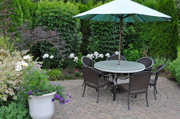 Patio table and umbrella in beautiful summer botanical garden - 写真・画像