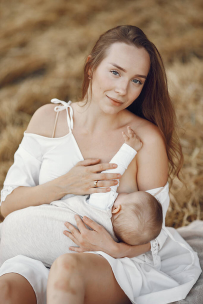 Mother with cute daughter. Mom breastfeeding her little daughter. Woman in a white dress. - Foto, Imagen